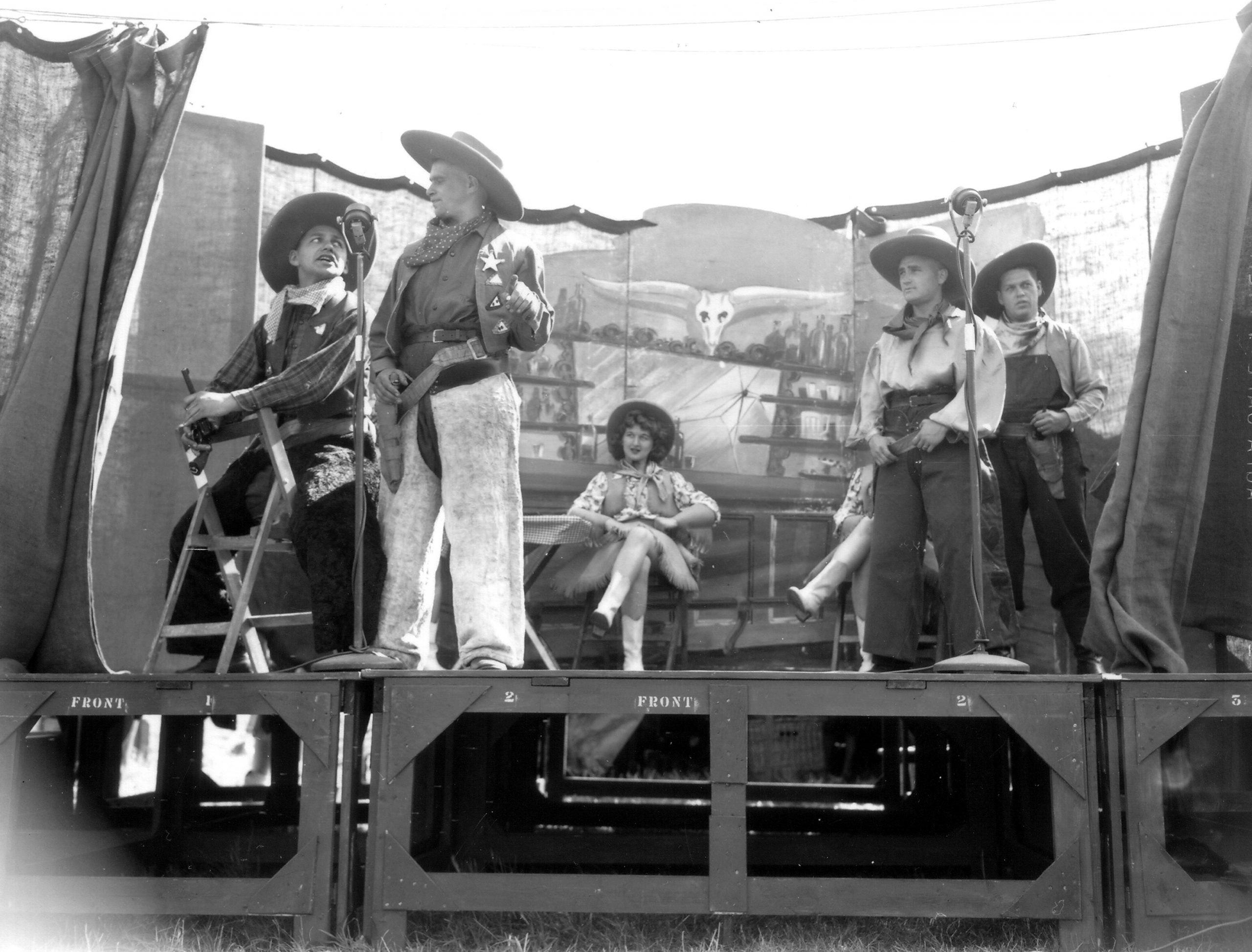 Sur une estrade des acteurs sont déguisés en cow-boys, à l'arrière-plan les danseuses sont assisses.
Reportage de 10 photos (p010871 à p010880) sur une représentation du spectacle de l'armée canadienne "Invasion Revue ", le 30 juillet 1944 à Banville.
http://www.flickr.com/search/?w=58897785%40N00&q=invasion%3A+revue%3B+canadien&m=text
Banville au sud de Graye-sur-Mer (secteur Juno) est libérée le 6 juin 1944 par les Canadiens. Le 25th  Airfield Construction Group, RE du 12th AGRE chargé de l'aménagement et de la réparation des terrains d'aviation de campagne était à Banville.
L'ALG B-3 est à proximité immédiate.